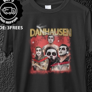 Könnte beinhalten: Schwarzes T-Shirt mit einer Grafik einer Gruppe von Personen mit Gesichtsbemalung und dem Wort "DANHAUSEN" in goldfarbenen Buchstaben. Das Bild hat einen Vintage-Look. Ein "BUY 3 FREE SHIPPING"-Logo befindet sich oben links.