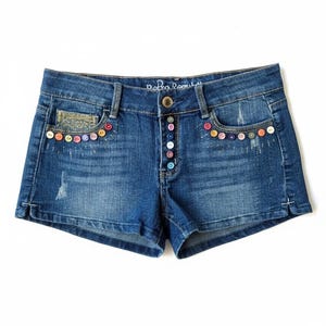 May include: Blue denim shorts with colorful button accents along the pockets and button fly. The shorts feature a distressed look with a faded wash and the text "Bobo Republic" above the button fly.