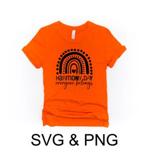 May include: An orange t-shirt featuring a black rainbow design and the text "HARMONY DAY everyone belongs". The shirt has a crew neck and short sleeves. The words "SVG & PNG" are below the shirt.
