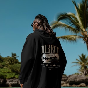 Puede incluir: Sudadera negra con la frase "DIRECT STATEMENT" y un diseño de cuchilla de afeitar en la espalda. La persona que la lleva tiene rastas y gafas de sol, con un fondo de palmeras y cielo azul.