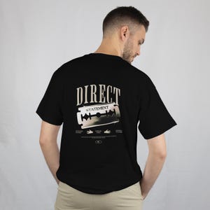 Puede incluir: Camiseta negra con la frase "DIRECT STATEMENT" y un gráfico de una cuchilla de afeitar. La camiseta tiene cuello redondo y mangas cortas. El diseño es de estilo vintage.