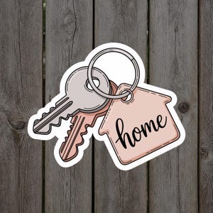 May include: A sticker featuring a set of keys and a house-shaped tag. The tag is light pink and has the word "home" written in a cursive font. The keys are silver and peach-colored, attached to a silver keyring.