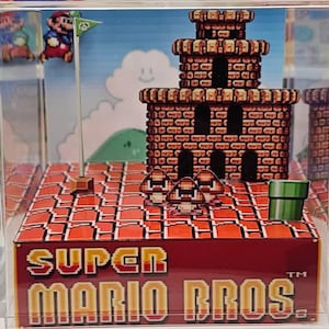 May include: A Super Mario Bros. diorama featuring a pixelated castle, flag, and characters. The base is red with the game's logo. A green pipe and mushroom characters are also present. The background shows a blue sky with a smiling cloud.