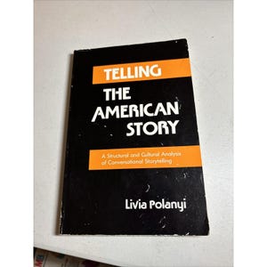 May include: A paperback book titled Telling The American Story: A Structural and Cultural Analysis of Conversational Storytelling by Livia Polanyi. The cover is black with orange horizontal bands and white text in a bold, sans-serif typeface.