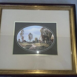 Pode incluir: Impressão emoldurada de uma paisagem rural com um caminho de terra, edifícios e árvores. A impressão está dentro de uma moldura oval, rodeada por uma borda dourada e envolta em uma moldura de madeira marrom escura e dourada.