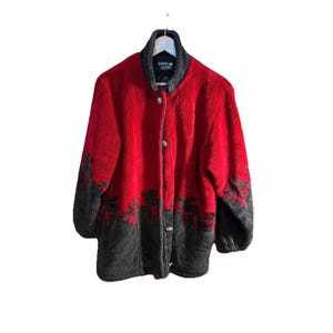 May include: A red and charcoal gray fleece jacket featuring a high collar and a button-front closure. The garment displays a repeating pattern of moose silhouettes along the lower section and sleeves, with a Nordic Lights brand label inside.