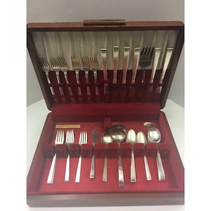 May include: A wooden silverware case with a red velvet interior, holding a complete set of silver-colored forks, knives, and spoons. The case is open, revealing the neatly arranged utensils. The label reads "Community Plate".