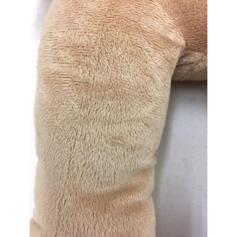 May include: Close-up of a plush, beige-colored stuffed animal. The fur is soft and textured, with a slight sheen. The image focuses on the details of the fabric and the gentle curves of the toy.