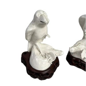 May include: White ceramic bird figurine perched on a rock, mounted on a dark brown wooden base. The bird has a detailed beak and feet. The figurine is a decorative item.