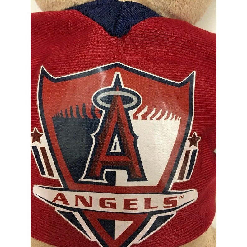 May include: A red jersey with the Los Angeles Angels logo, featuring a large white "A" with a halo and the word "ANGELS" below. The jersey has a navy blue collar.