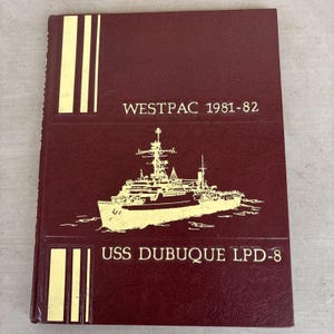 May include: A maroon hardcover book with a textured finish featuring gold foil lettering and a gold illustration of a naval ship. The cover text reads WESTPAC 1981-82 and USS DUBUQUE LPD-8, accompanied by three vertical gold stripes in the corners.