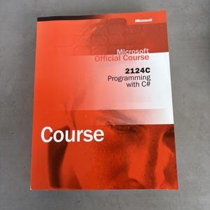 Könnte beinhalten: Ein rechteckiges Schulungshandbuch mit dem Titel Microsoft Official Course 2124C Programming with C#. Das Cover zeigt ein leuchtendes orange-weißes Verlaufsdesign mit einer schwachen Grafik eines menschlichen Gesichts und dem Wort Course.