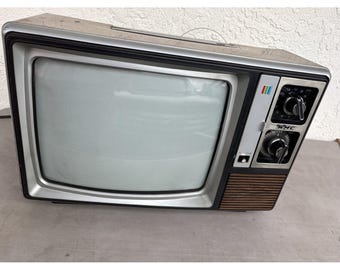 May include: Vintage KMC television with a silver frame and a brown wooden speaker panel. The TV has two control knobs and a power button on the front. The screen is blank and gray. A retro electronic device.