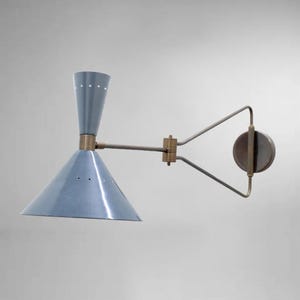 May include: A wall-mounted light fitting with a light blue conical shade and a cylindrical top. The fitting has a brass-coloured arm and a circular backplate. The shade has small, evenly spaced holes.