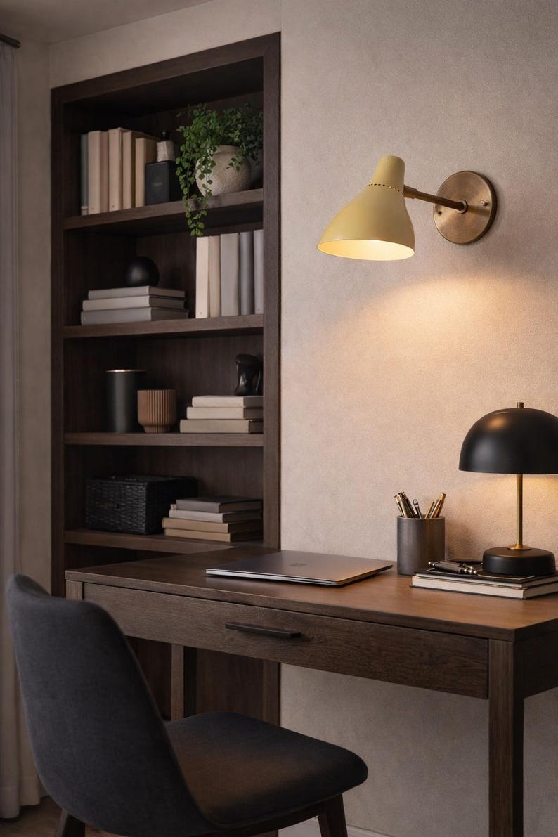 May include: A home office setup with a dark wood desk, chair, and built-in bookshelf. A yellow wall-mounted lamp and a black desk lamp provide light. The desk holds a laptop, pens, and books. A small plant sits on the bookshelf.