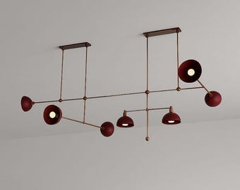 May include: A modern, multi-light ceiling fixture with a linear design. It features several maroon-colored, dome-shaped lights attached to a network of bronze-colored rods and supports. The fixture is designed to be mounted on a ceiling.