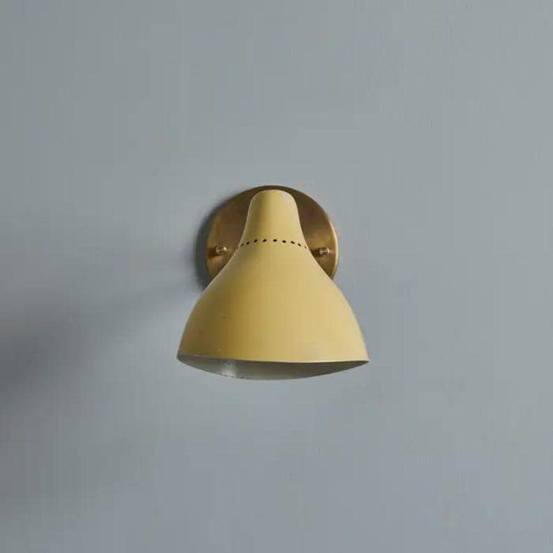 May include: A yellow wall sconce with a brass-colored mounting plate. The sconce has a conical shade with a series of small holes near the top. The fixture is mounted on a light blue wall.