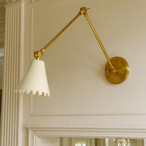 May include: A wall-mounted brass swing arm lamp with a white, scalloped shade. The lamp has a circular base and adjustable arm, suitable for reading or task lighting. The design is classic and elegant.