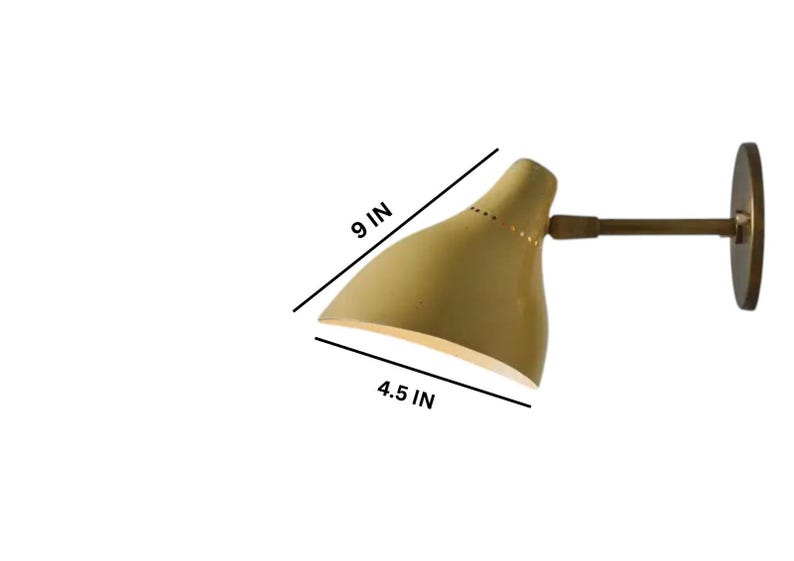 May include: A wall-mounted lamp with a pale yellow shade, measuring 9 inches long and 4.5 inches wide. The lamp has a brass arm and a circular mounting plate. The shade has small perforations along the top edge.
