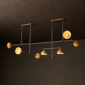 May include: A contemporary ceiling light fixture with a brass finish. It features several off-white, circular and dome-shaped shades, each with a light bulb. The design is geometric and minimalist, suitable for a modern interior.