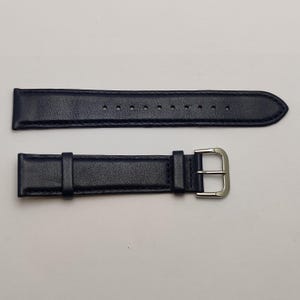May include: A navy blue watch strap with a silver-colored buckle. The strap is made of a smooth, leather-like material and features several holes for adjustment. The watch band is designed to be attached to a watch face.