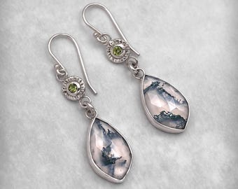 May include: Silver dangle earrings featuring teardrop-shaped gemstones with a white and green pattern. Each earring has a small green gemstone and a decorative silver setting. The earrings are designed with a hook closure.