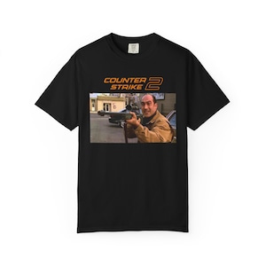 May include: Black t-shirt featuring the text "COUNTER STRIKE 2" in orange. The shirt has a graphic of a man holding a rifle. The image is a still from a movie or video game.
