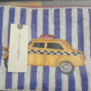 May include: Beaded pouch with a yellow taxi cab design on a blue and white striped background. The pouch has a zipper closure and a tag that says Anthropologie.