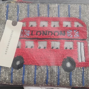 May include: A beaded clutch featuring a red double-decker bus design with the word "LONDON" and Union Jack flags. The bag has a silver and blue striped background and a tag that reads "ANTHROPOLOGIE".