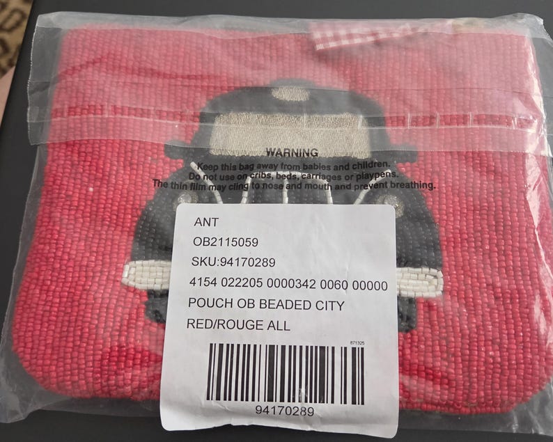 May include: A red beaded pouch with a black and beige design. The pouch is in a clear plastic bag. The pouch has a beaded design of a vehicle. The pouch has a tag with text.