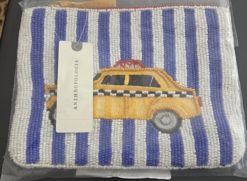 May include: Beaded clutch with a vertical striped pattern in white and blue. A yellow taxi cab design is embroidered on the front. The tag reads ANTHROPOLOGIE.
