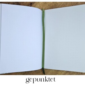Puede incluir: Diario de cuadr&iacute;cula de puntos abierto con cubiertas estampadas florales y un marcador de cinta verde. Las p&aacute;ginas est&aacute;n en blanco con un patr&oacute;n de cuadr&iacute;cula de puntos. La palabra "gepunktet" est&aacute; escrita en la parte inferior de la imagen.