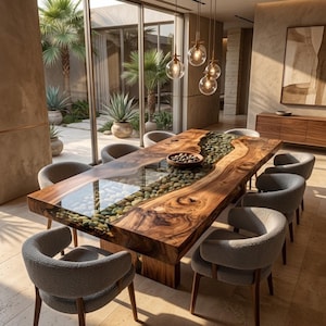 May include: A rectangular dining table featuring a live-edge wood slab with a central glass inlay filled with smooth river stones. The table is surrounded by eight grey upholstered chairs with curved backrests and wooden legs in a bright room.