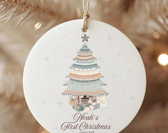 May include: Round Christmas ornament with a decorative Christmas tree design in pastel colors. The tree is topped with a star and surrounded by gifts and a teddy bear. The text "Noah's First Christmas 2025" is printed below the tree.