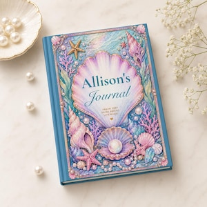 May include: A blue journal with a seashell design. The cover features a large, pearlescent seashell with the text "Allison's Journal" and the words "Dream Deep, Shine Bright, Live Magic." The design includes starfish, pearls, and other seashells.