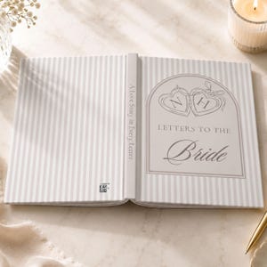 Puede incluir: Libro abierto con un patr&oacute;n de rayas grises y blancas. La portada dice "A Love Story in Every Letter". La p&aacute;gina derecha presenta el texto "Letters to the Bride" con dos dise&ntilde;os en forma de coraz&oacute;n, cada uno con una letra en su interior.