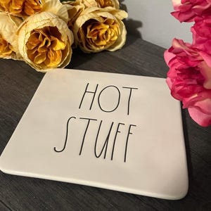 May include: A white, rectangular ceramic tray with rounded corners. The words "HOT STUFF" are written in black, handwritten-style lettering. The tray is surrounded by yellow and pink flowers.