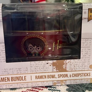 May include: A boxed ramen bowl set featuring a cartoon image of a character with glasses. The bowl is red with gold accents and the name "Harry" in gold lettering. The packaging reads "RAMEN BOWL, SPOON, & CHOPSTICKS".