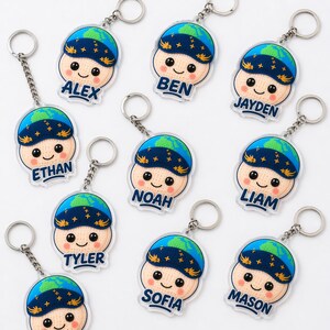 May include: A collection of personalized keychains featuring a smiling cartoon character with a blue and green globe-shaped hat. Each keychain has a different name: Alex, Ben, Ethan, Noah, Jayden, Liam, Tyler, Sofia, and Mason. The keychains have a silver chain and ring.