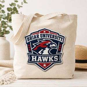 May include: A beige canvas tote bag featuring a Briar University Hawks emblem. The emblem is a shield shape with the words "Briar University" and "Hawks" in white text, and a red and blue hawk graphic.