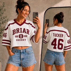A woman wearing a white and maroon hockey jersey with the number 46, taking a selfie in front of a mirror.
