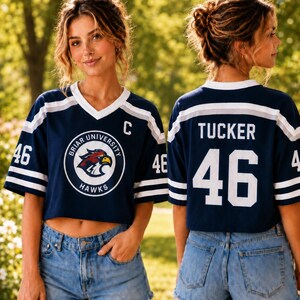 A young woman wearing a navy blue crop top with a white and navy blue logo, a white "C" on the front, and the number 46, posing outdoors in denim shorts.