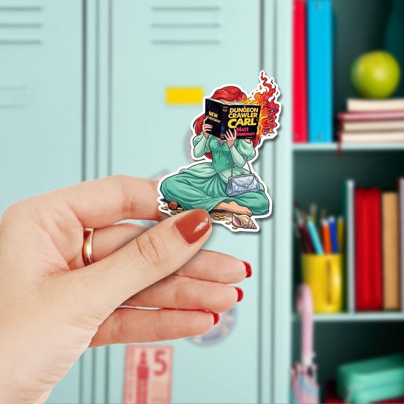 A hand holding a sticker of a cartoon girl reading a book, with flames coming out of the book.