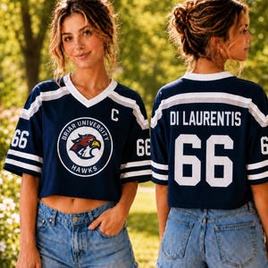 A young woman wearing a navy blue crop top with a white and navy blue design, a white "BIER UNIVERSITY HAWKS" logo, and denim shorts.
