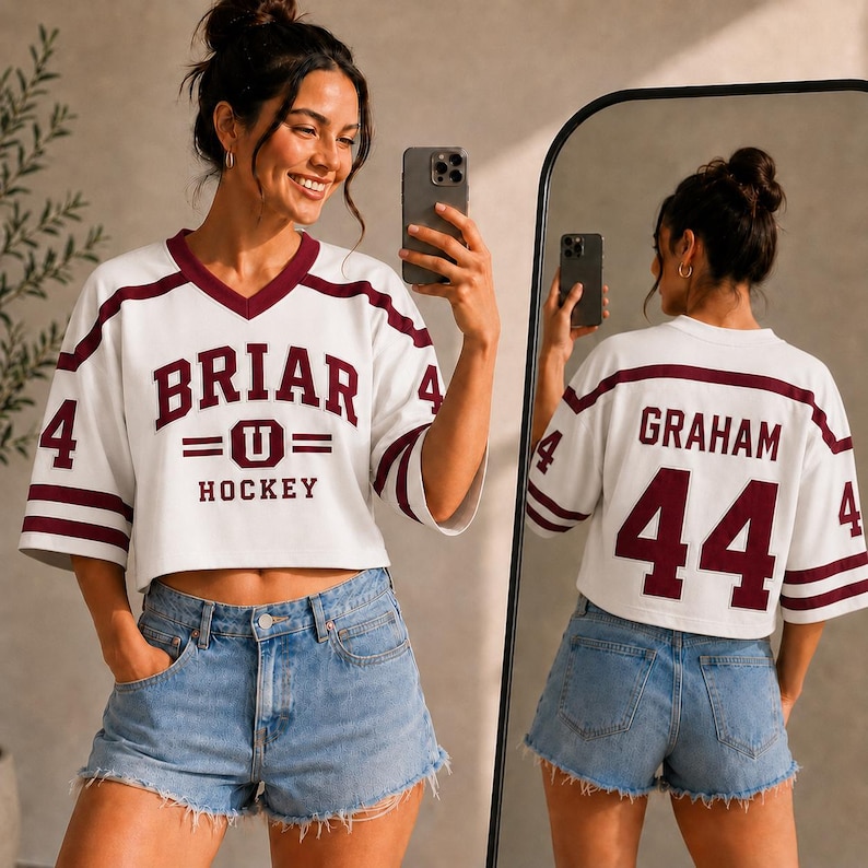 A woman wearing a white hockey jersey with the number 44 and the name Graham, taking a selfie in front of a mirror.