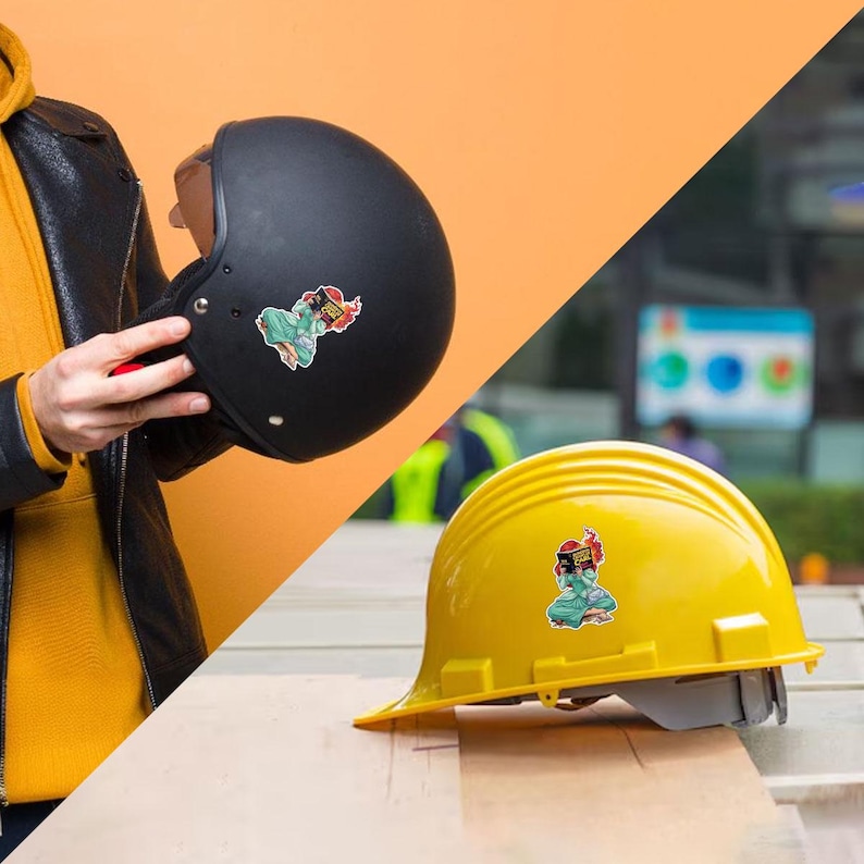 a person holding a black motorcycle helmet and a yellow construction helmet with stickers on them, both placed on a wooden surface.