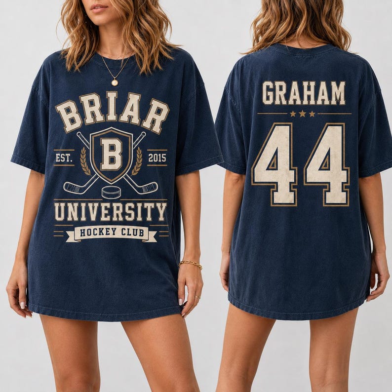A navy blue t-shirt with a graphic design featuring the text "BRIAR UNIVERSITY HOCKEY CLUB" and the number "44". The design also includes a shield-shaped emblem with a hockey stick and a hockey puck.