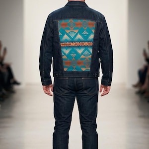 May include: A dark wash denim jacket and jeans ensemble. The jacket features a colorful geometric pattern on the back in shades of teal, orange, and cream. The model is wearing black shoes.