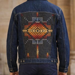 May include: A dark wash denim jacket with a patterned back panel. The panel features a geometric design in shades of orange, yellow, red, and blue on a gray background. The jacket has a classic collar, button closures, and pockets.