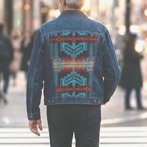 May include: A white ceramic mug with a black handle and the text "But First, Coffee" in a bold, black font. The mug is set against a blurred background, suggesting a cozy setting.